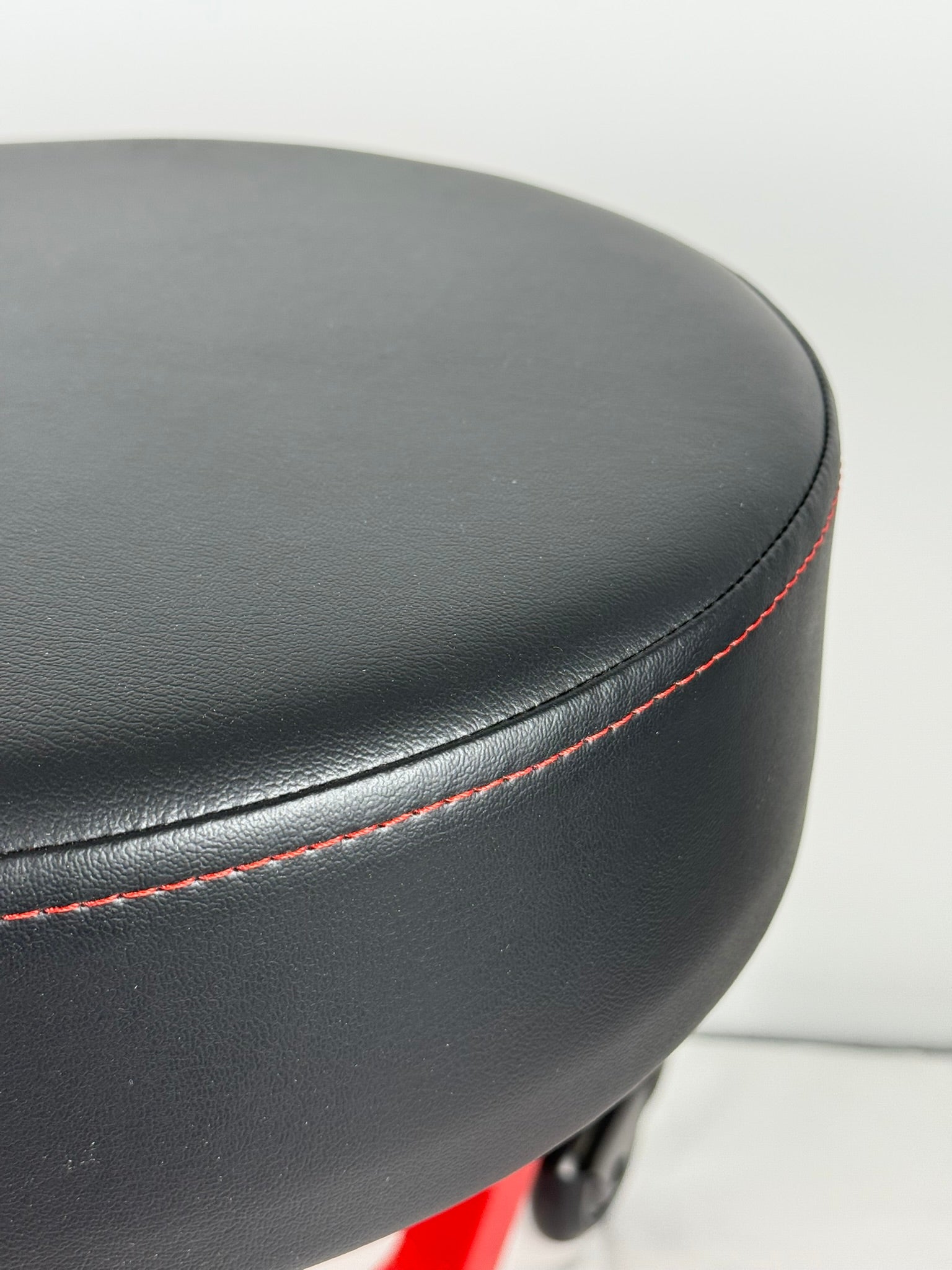 Close-up of a black leather stool with red stitching on a white background