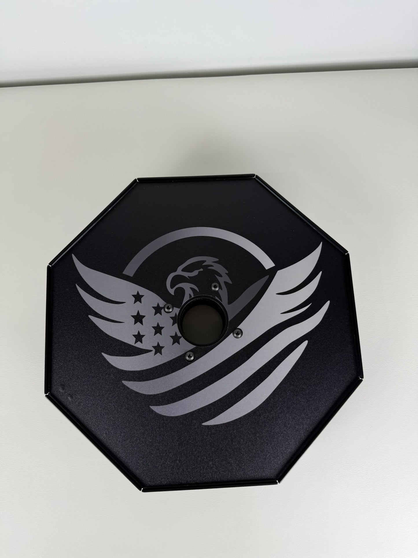 Black octagonal object with gray eagle and star design on a white background
